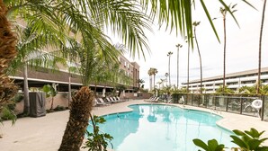 Una piscina con sillones de descanso, palmeras y un edificio al fondo.