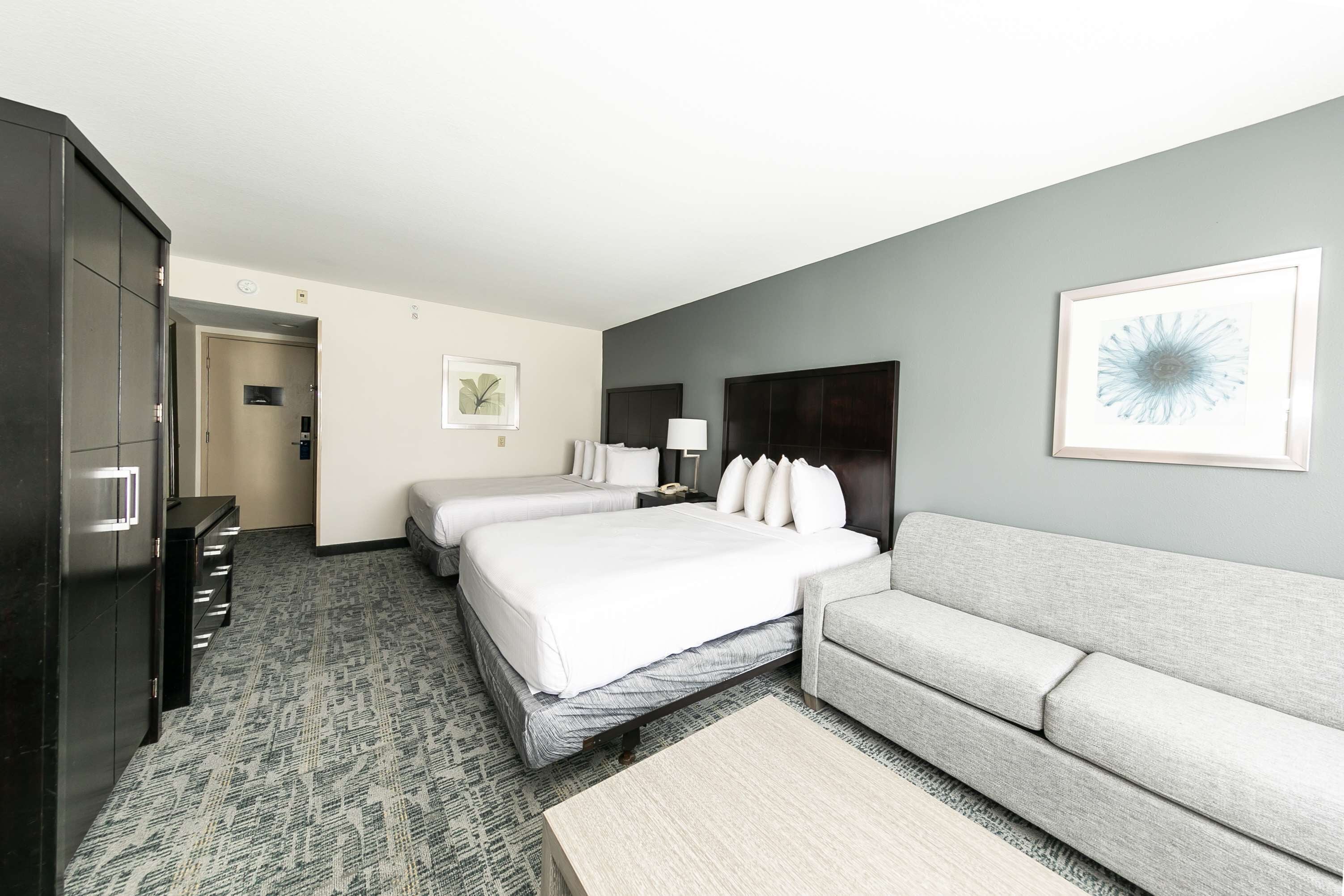 A hotel room with two beds, a gray sofa, a wooden coffee table, and a dark wardrobe.