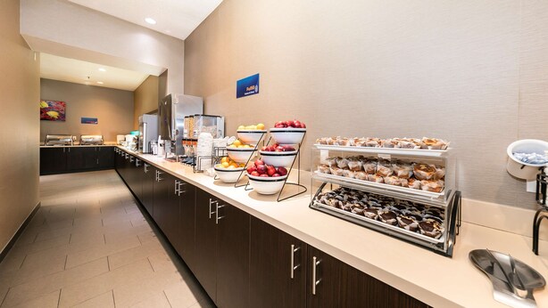 Zona de desayuno de hotel con una larga barra que exhibe diversas opciones de comida, como frutas, pastelería y una estación de café.