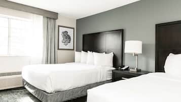 A hotel room with two beds, a dark headboard, a bedside table with a lamp, and a framed picture on the wall.