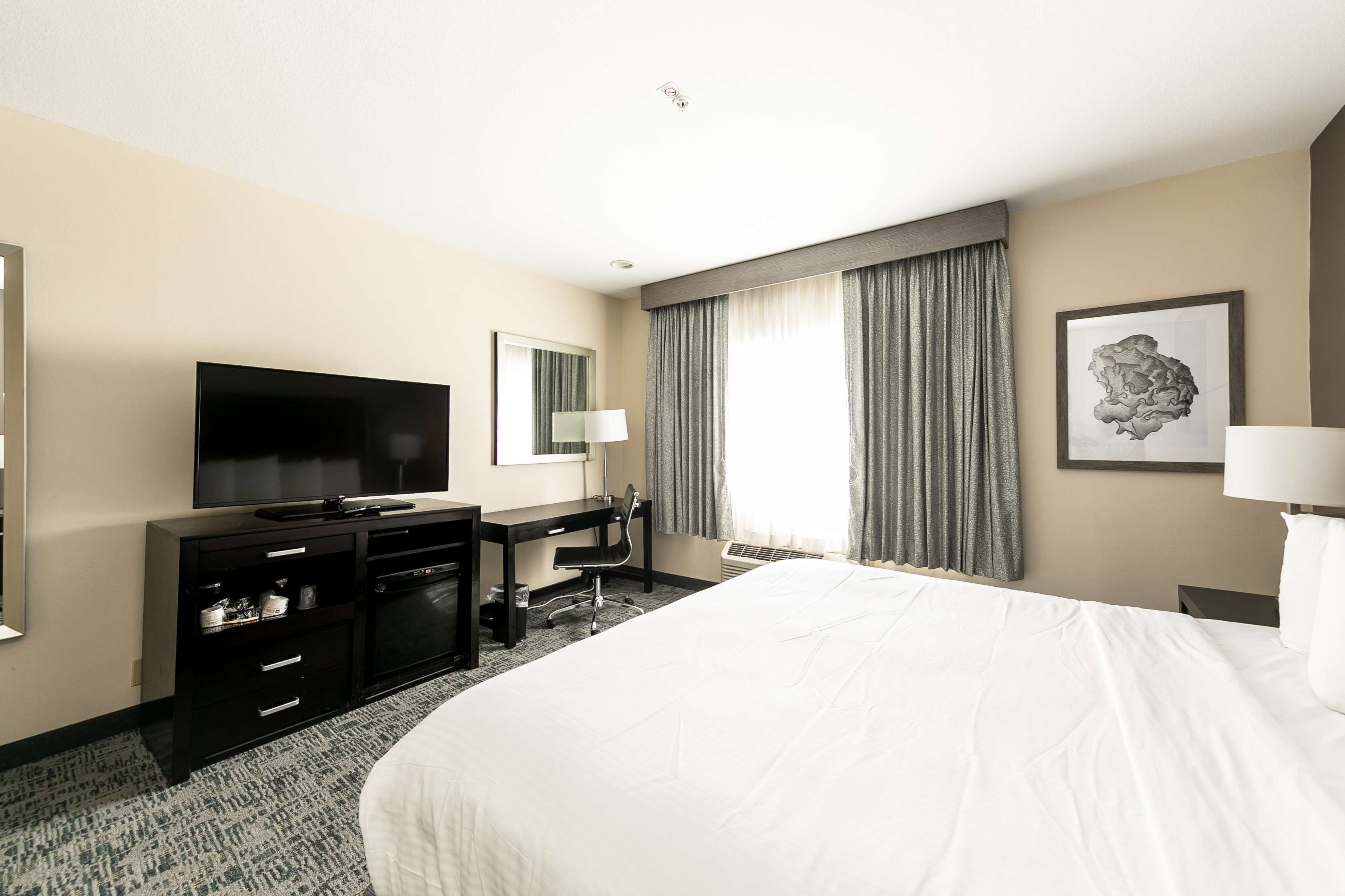 Een hotelkamer met een groot bed, een flatscreen televisie, een bureau met een stoel en een groot raam met gordijnen.