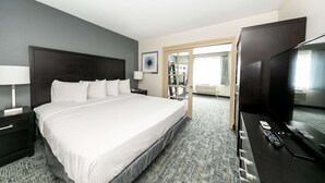 Una habitación de hotel con una cama grande, un televisor, un escritorio con lámpara y una estantería.