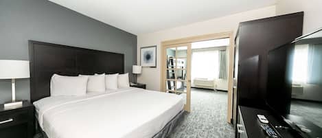 Una habitación de hotel con una cama grande, un televisor, un escritorio con lámpara y una estantería.