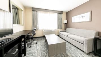 A hotel room with a sofa, a desk with drawers, a television, and a window with curtains.