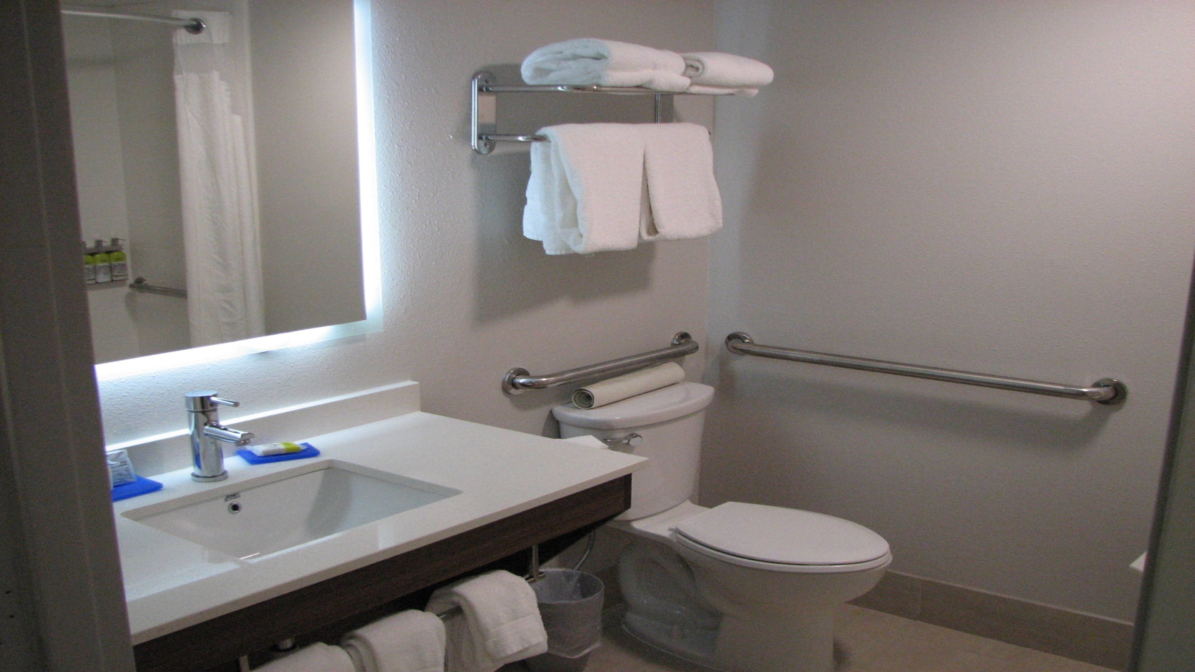 A bathroom with a white sink, mirror, and toilet. There is a towel rack above the toilet and a grab bar next to it.