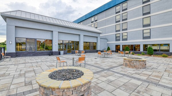 A courtyard with outdoor seating, a fire pit, and a building with large windows and a blue awning.