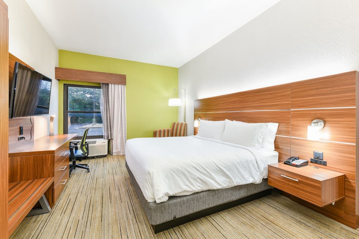 A hotel room with a bed, bedside table, desk, chair, and a window with curtains.