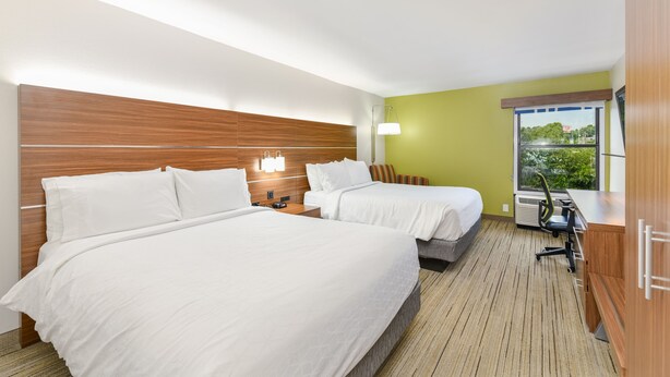 Une chambre d’hôtel avec deux lits, un bureau, une chaise, une lampe et une fenêtre donnant sur un beau paysage.