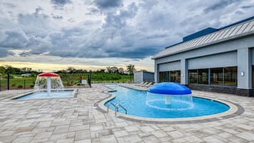 Une piscine dotée de deux éléments décoratifs aquatiques, d’un espace abrité et d’un bâtiment avec de grandes fenêtres.