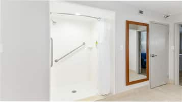 Une salle de bain avec une douche à l’italienne, une barre d’appui, un miroir et une porte.