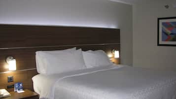 A hotel room with a large bed, two bedside tables, a nightstand, a wall-mounted lamp, and a framed picture.