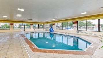 An indoor swimming pool with clear glass walls, tiled flooring, and a blue pool cover.