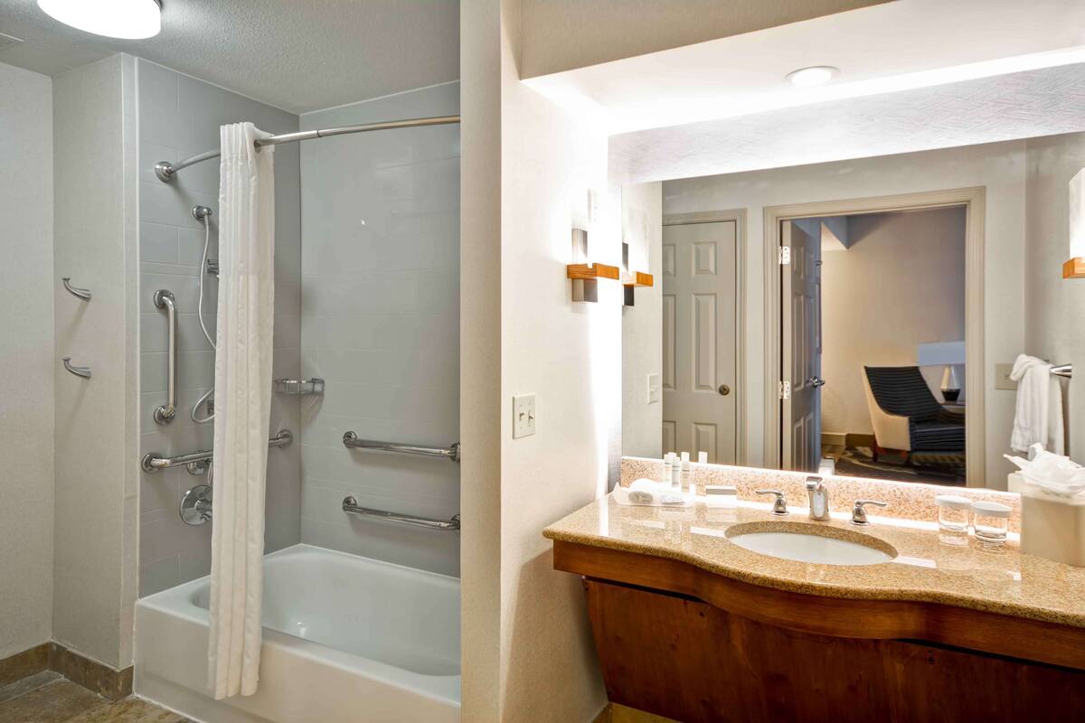 A bathroom with a bathtub, shower, and vanity with a sink and mirror.