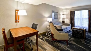 A hotel room with a wooden dining table, two chairs, a sofa, a small side table, a lamp, and a window with curtains. - Homewood Suites by Hilton San Antonio Northwest (San Antonio)