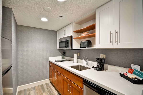Una cocina moderna con armarios blancos, un microondas de acero inoxidable, una cafetera y un lavavajillas.