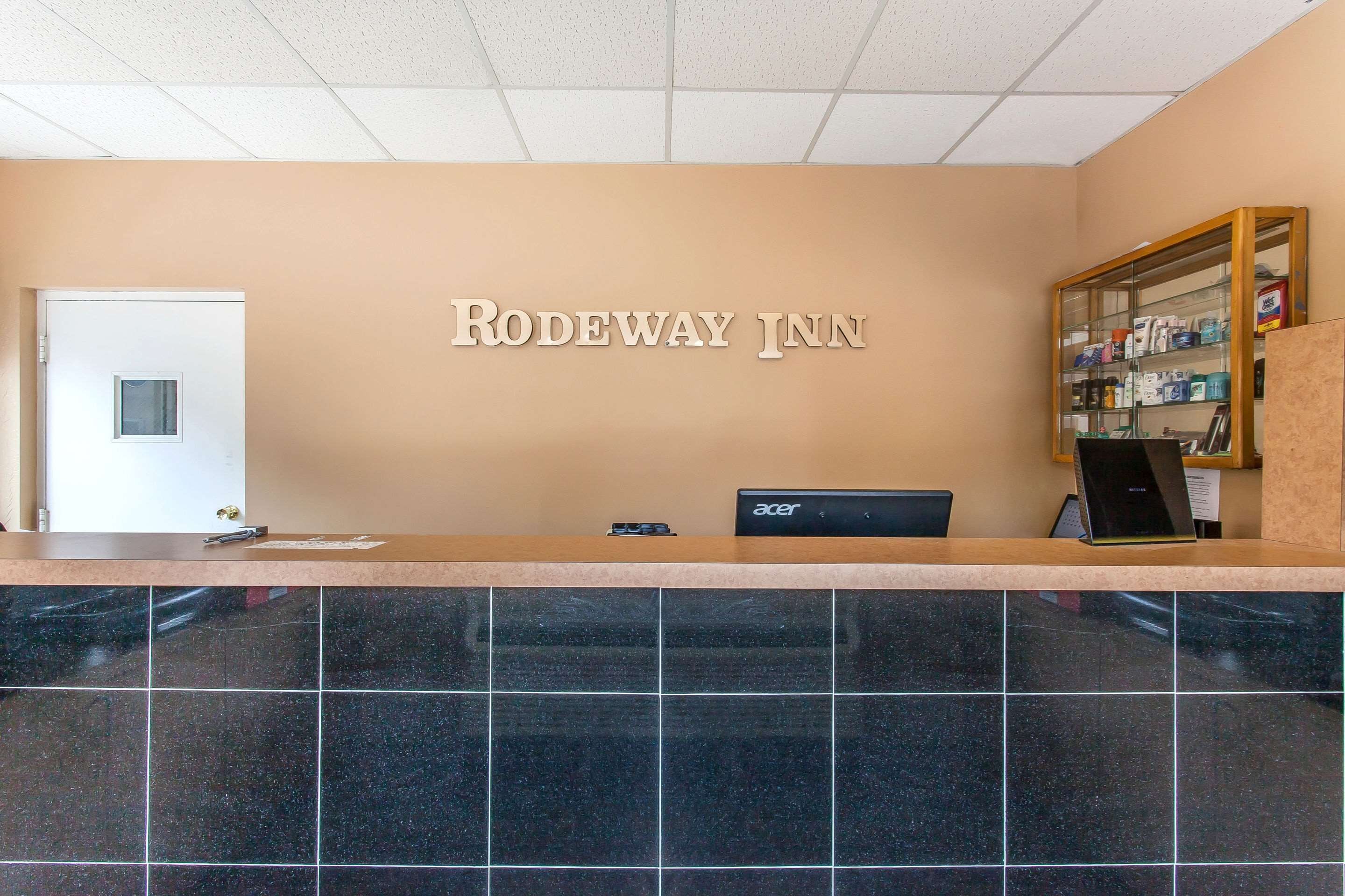 Una recepción en Rodeway Inn con una placa identificativa, una computadora y una vitrina con artículos de aseo.