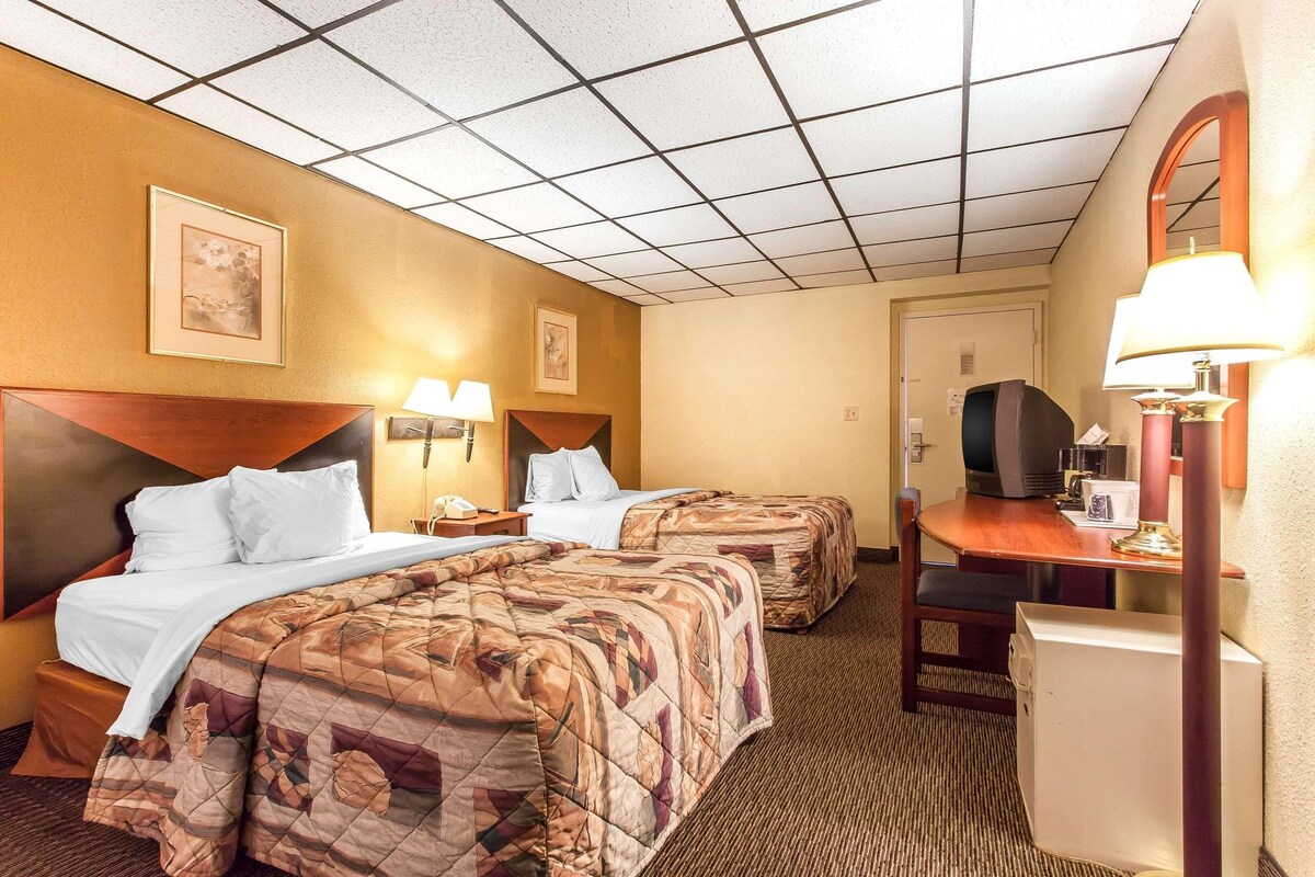 Habitación de hotel con dos camas, un escritorio y una silla. Hay lámparas en el escritorio y lámparas fijadas a la pared sobre las camas.