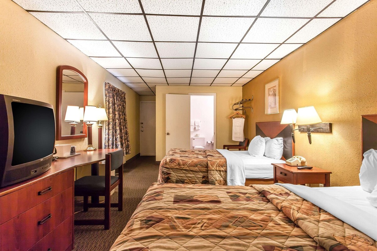 Habitación de hotel con dos camas, un escritorio con televisor, un espejo y dos mesitas de noche con lámparas.