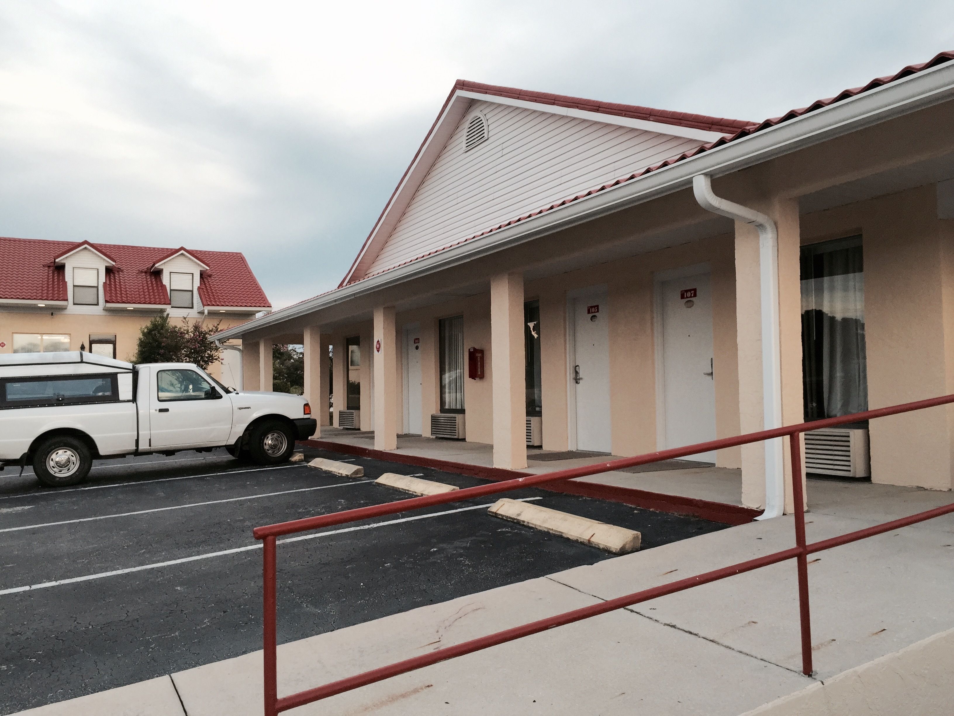Un motel doté d’un parking couvert et d’un camion blanc stationné à l’extérieur.