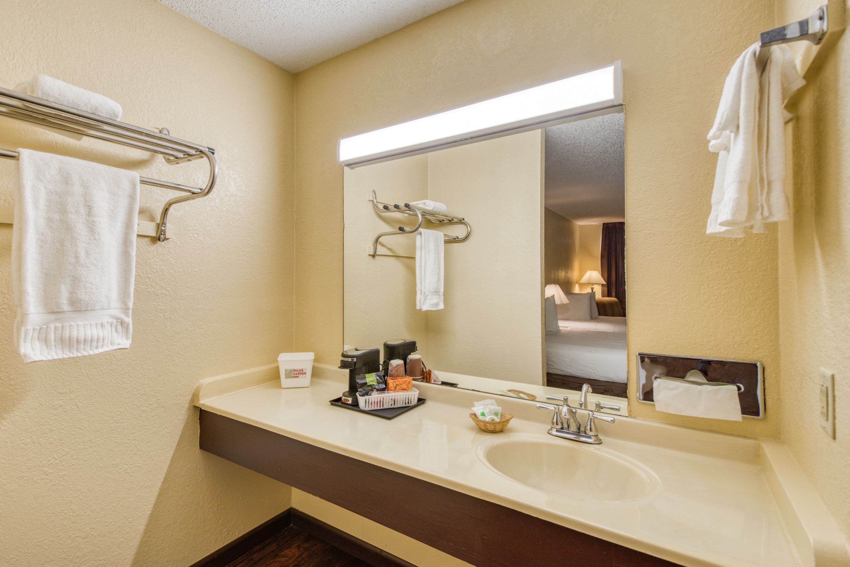 A hotel bathroom with a large mirror, a sink, and towel racks.