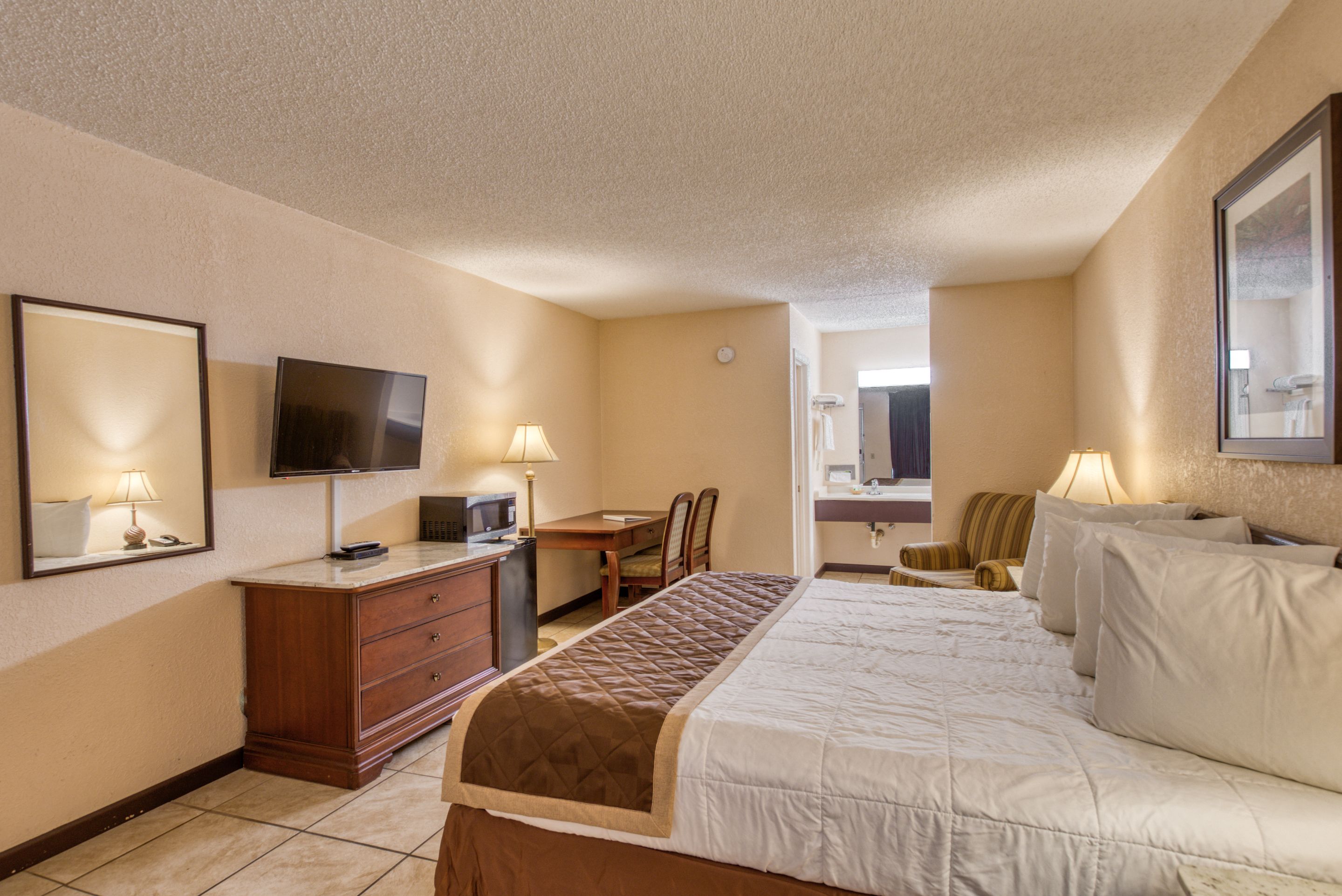 A hotel room with a bed, a desk, a chair, a TV, and a mirror.