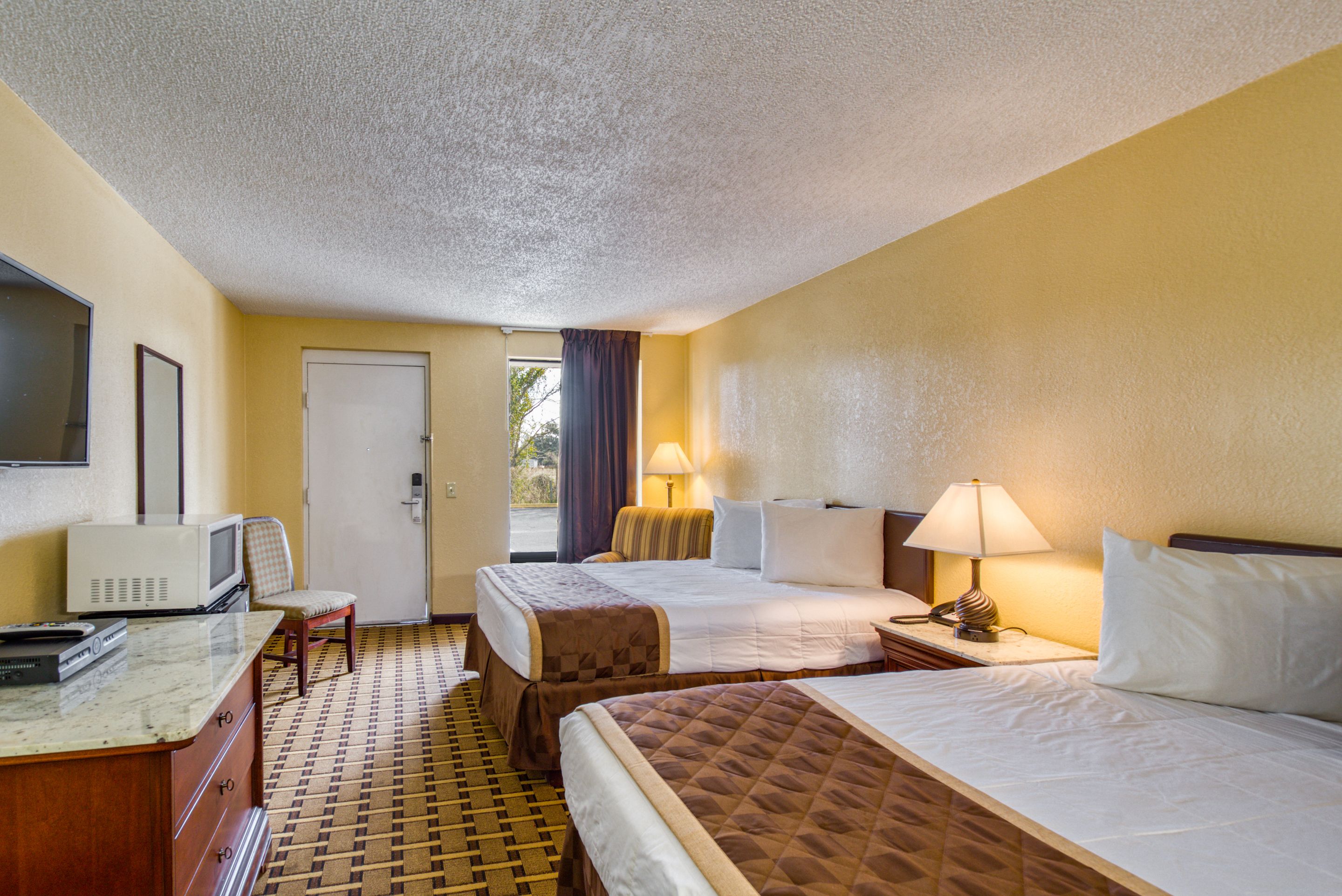 Une chambre d’hôtel avec deux lits, un bureau avec une télévision et une fenêtre avec des rideaux.