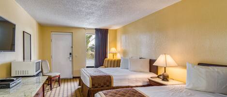 A hotel room with two beds, a desk with a television, and a window with curtains.