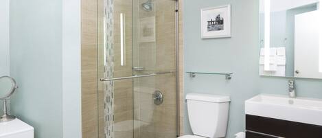 A bathroom with a glass-enclosed shower, a toilet, a sink, and a mirror.