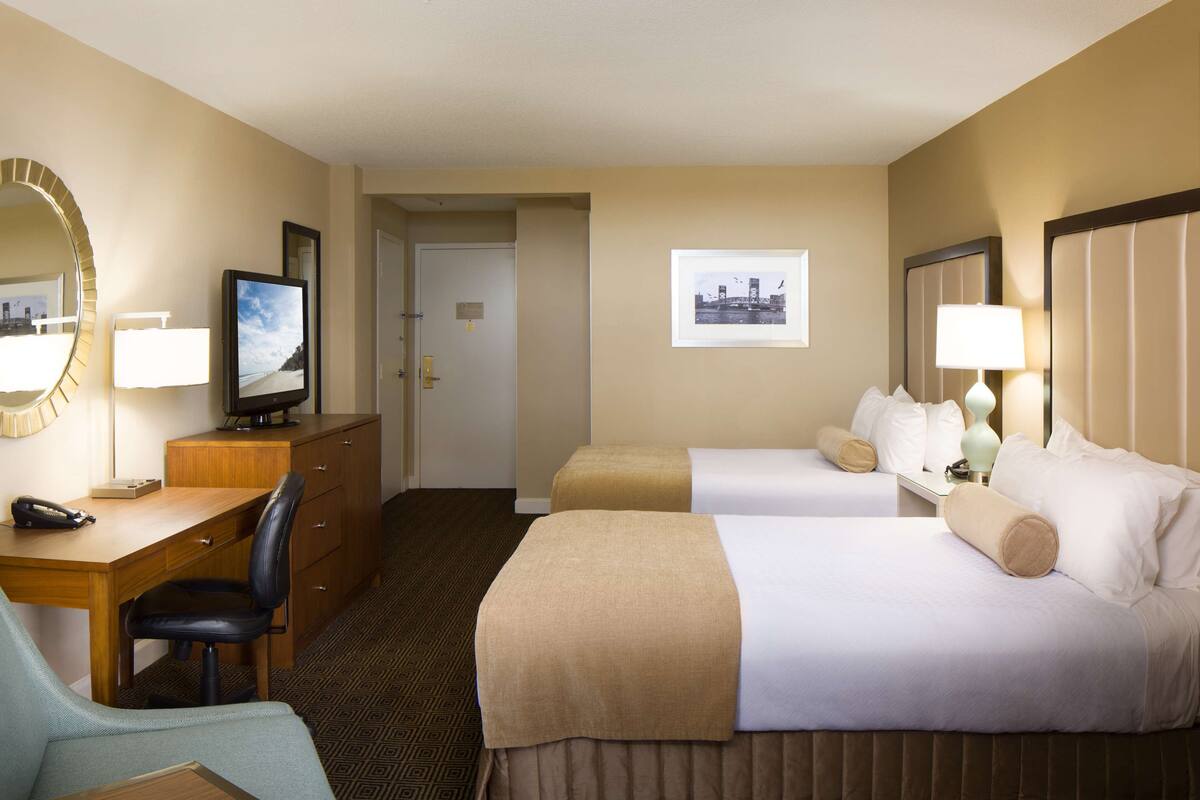 Une chambre d’hôtel avec deux lits, un bureau avec une chaise, une télévision et un miroir.