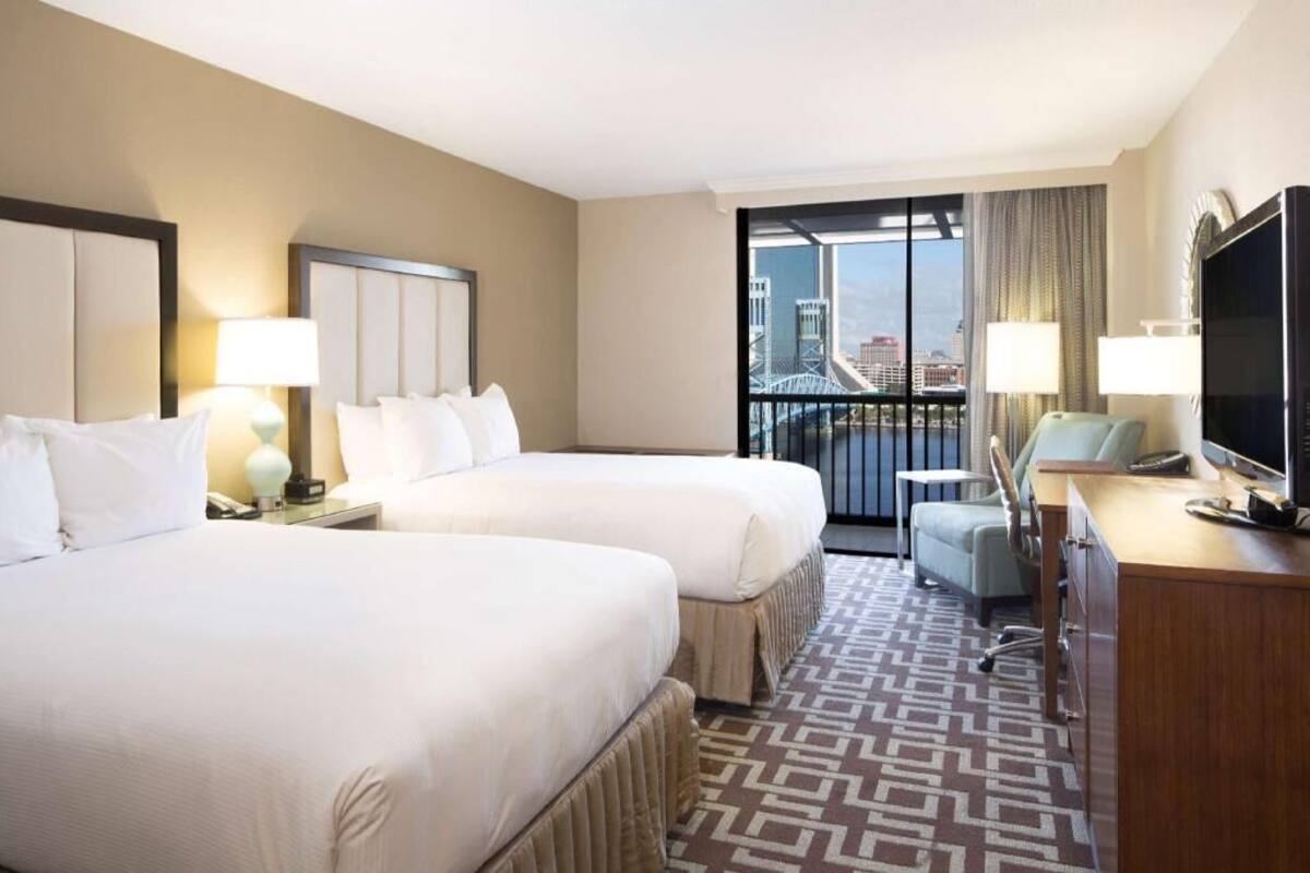 Une chambre d’hôtel avec deux lits, un bureau, une télévision et une vue sur un pont et le paysage urbain.