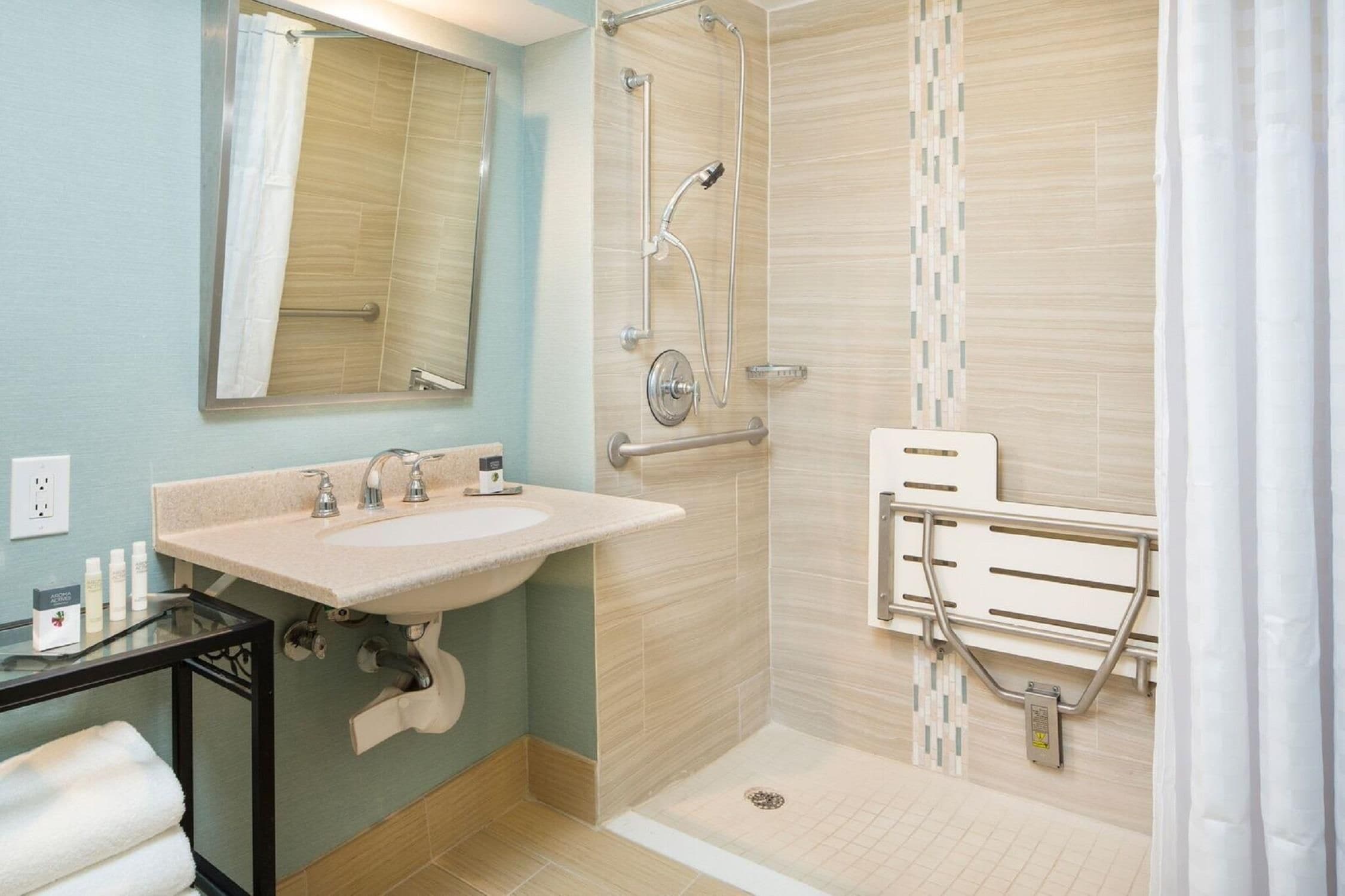 Un baño con lavamanos, espejo, ducha y barras de apoyo.