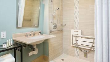 Un baño con lavamanos, espejo, ducha y barras de apoyo.