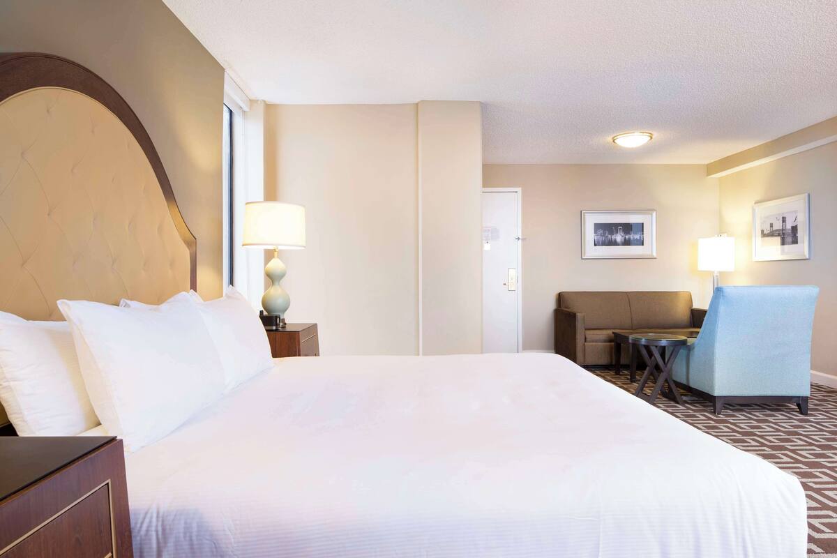 Une chambre d’hôtel avec un grand lit, un canapé, un fauteuil, une petite table et deux lampes.