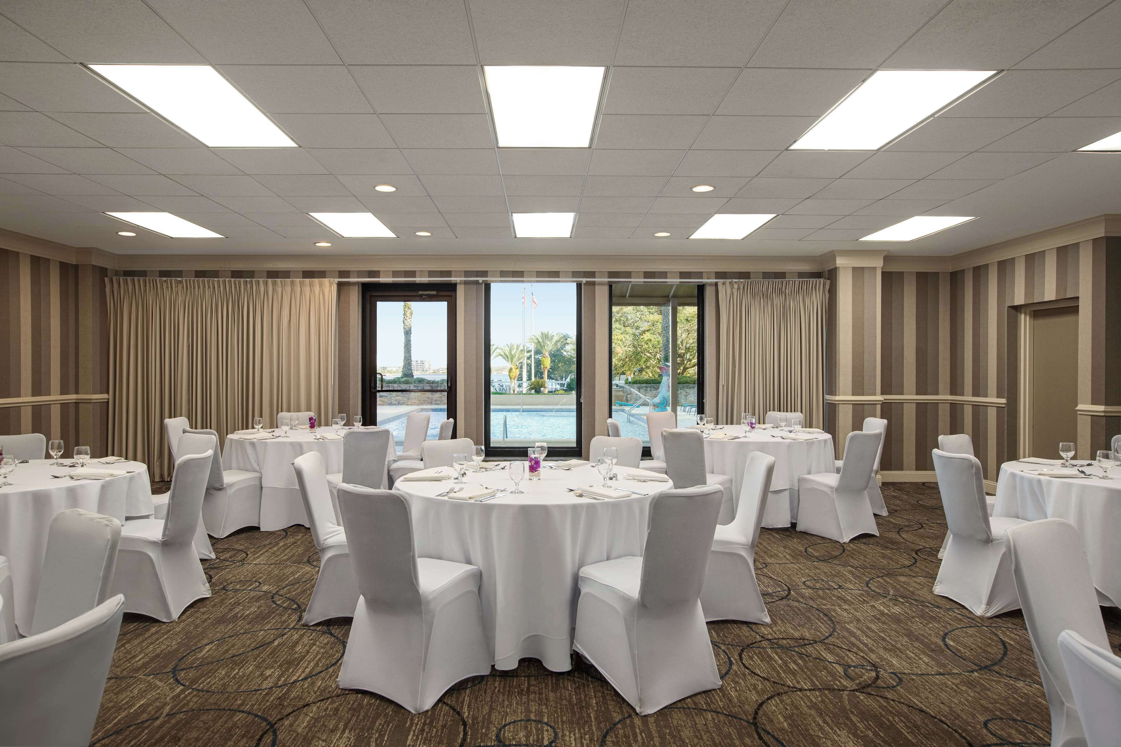 A conference room with round tables, white chairs, and a carpeted floor.