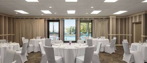 A conference room with round tables, white chairs, and a carpeted floor.