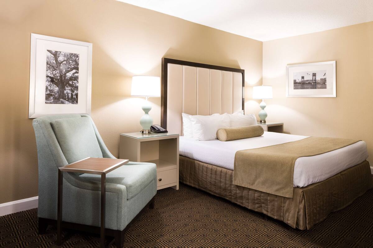 Une chambre d’hôtel comprenant un lit, une chaise, une table de chevet et deux lampes fixées au mur.