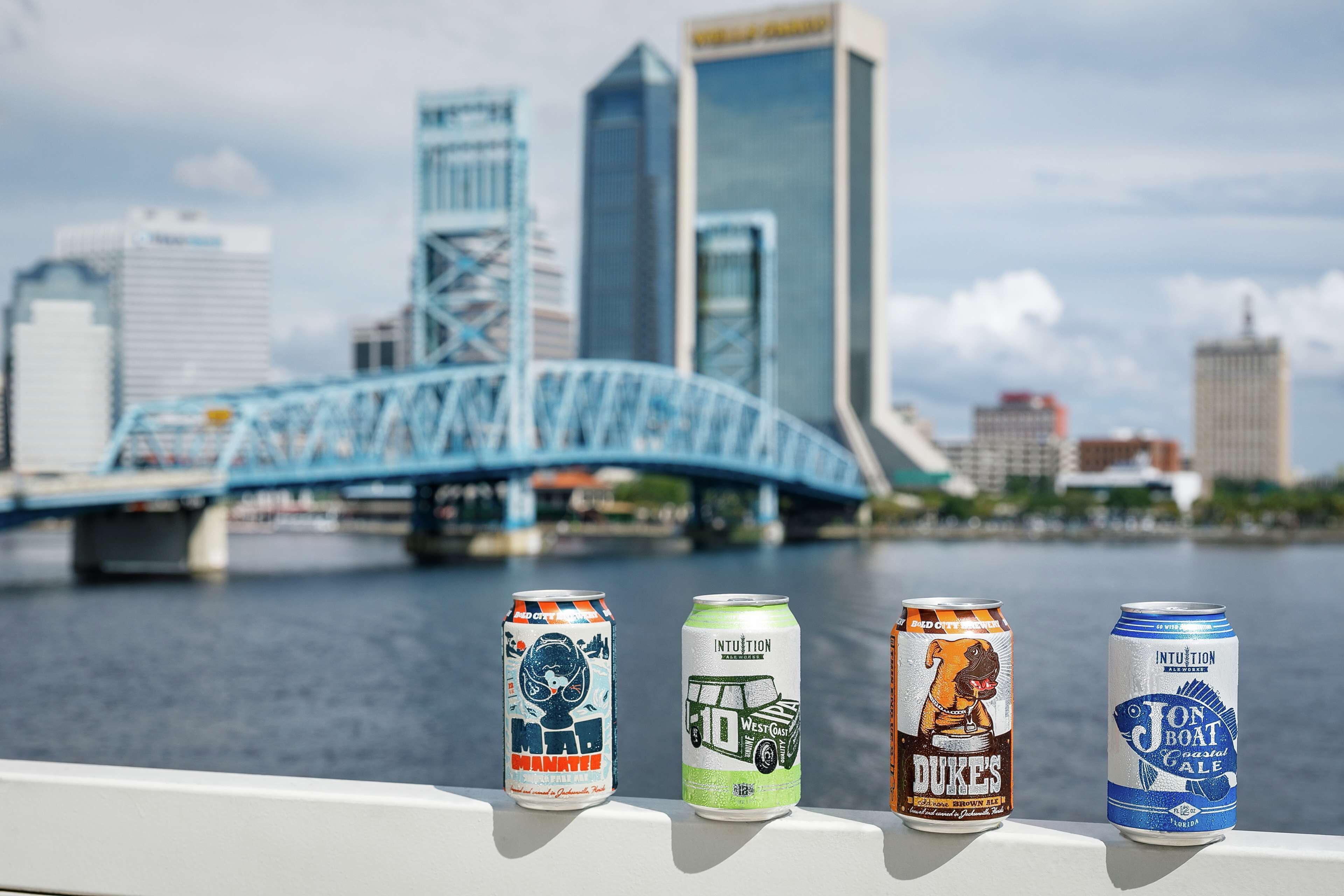 Vier blikjes bier op een leuning, met een stadszicht en een brug op de achtergrond.