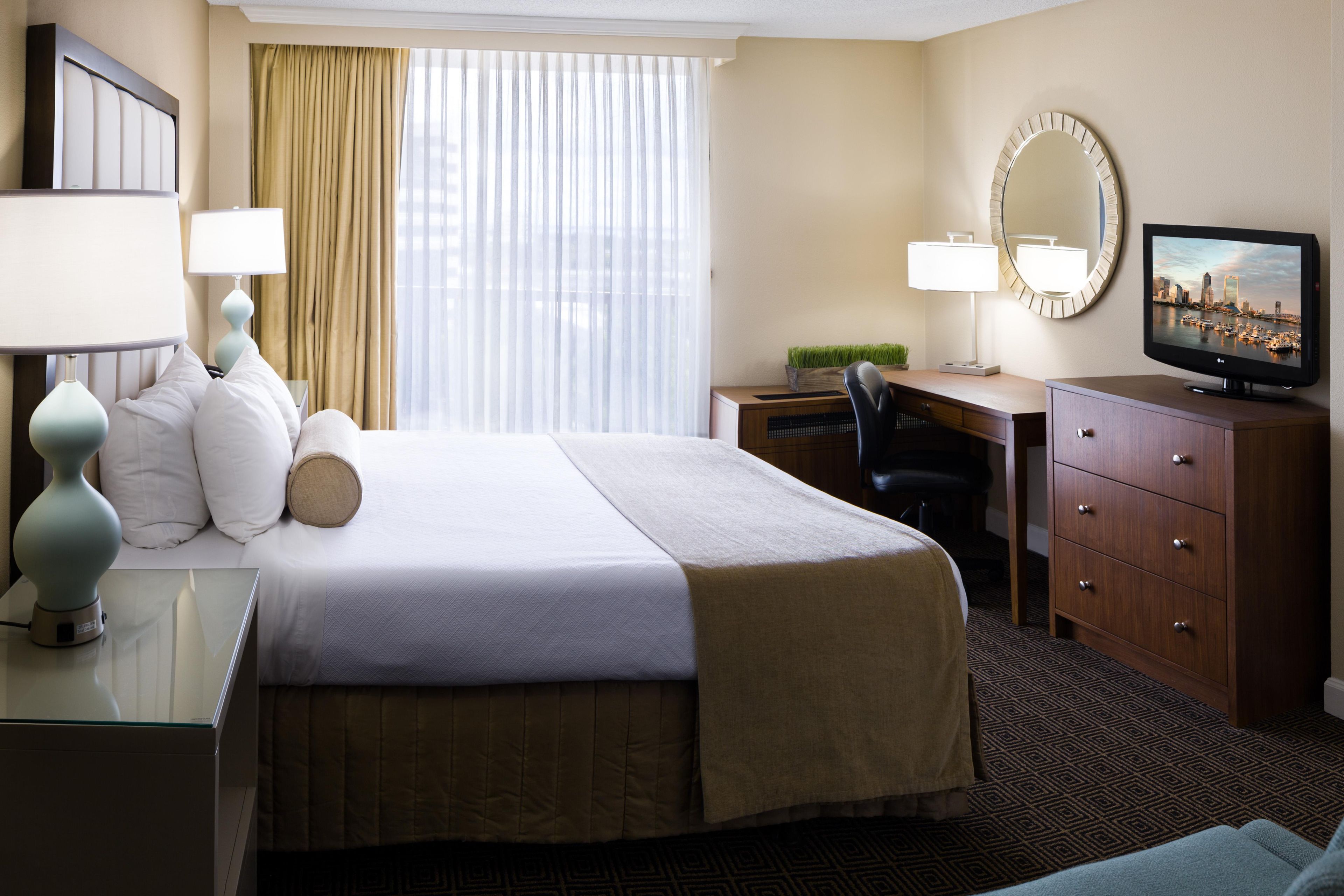A hotel room with a large bed, a desk, a chair, a television, and a mirror.