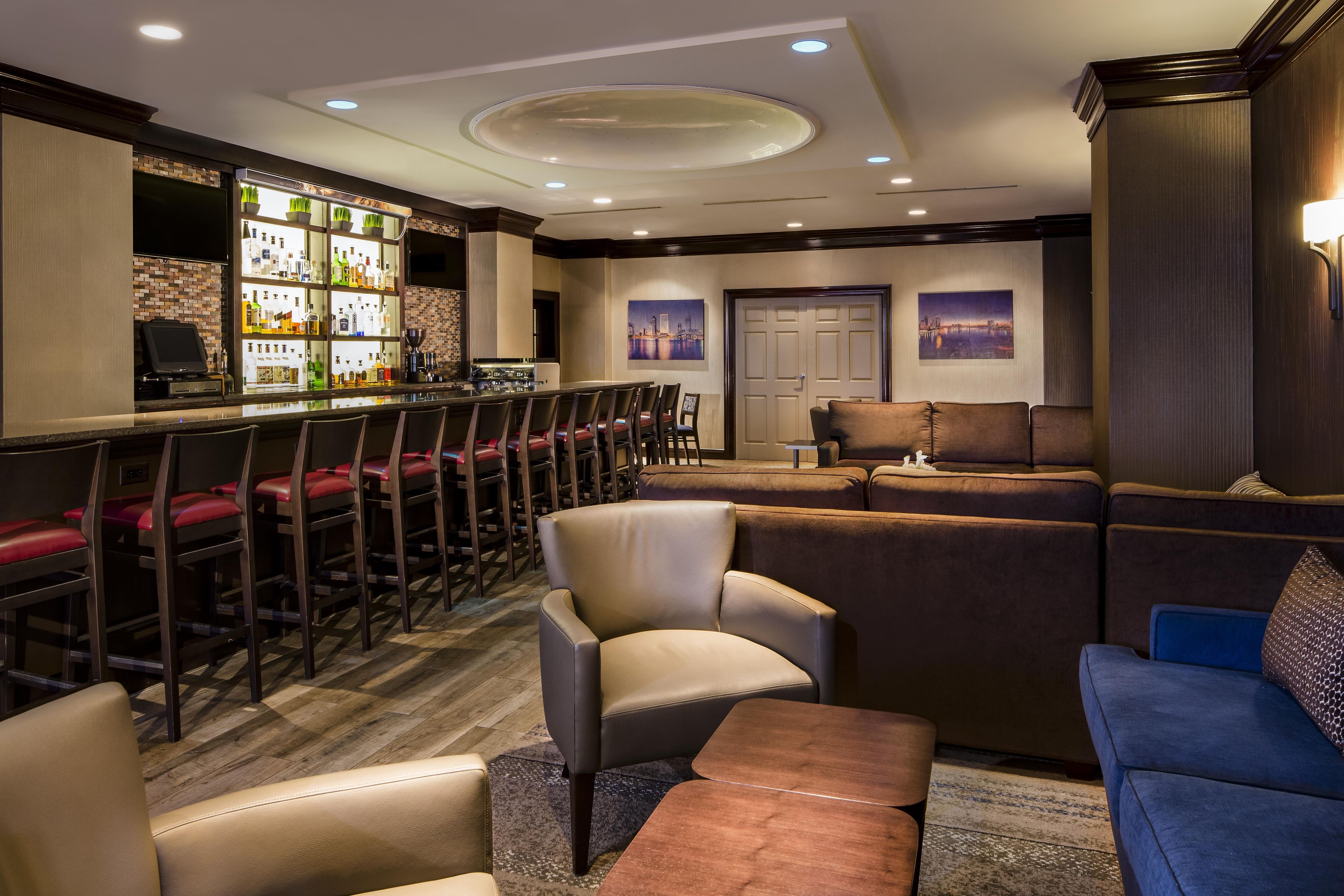 A bar area with a long counter, multiple bar stools, and a seating area with sofas and chairs.