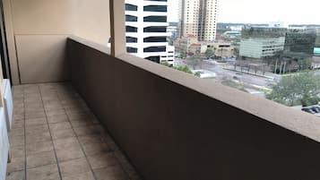A balcony with a tiled floor and a view of a cityscape including tall buildings and a parking area.