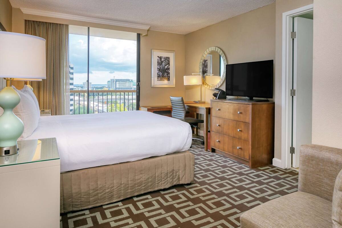 Une chambre d’hôtel avec un grand lit, un bureau avec une chaise, une télévision et une vue sur la ville par la fenêtre.