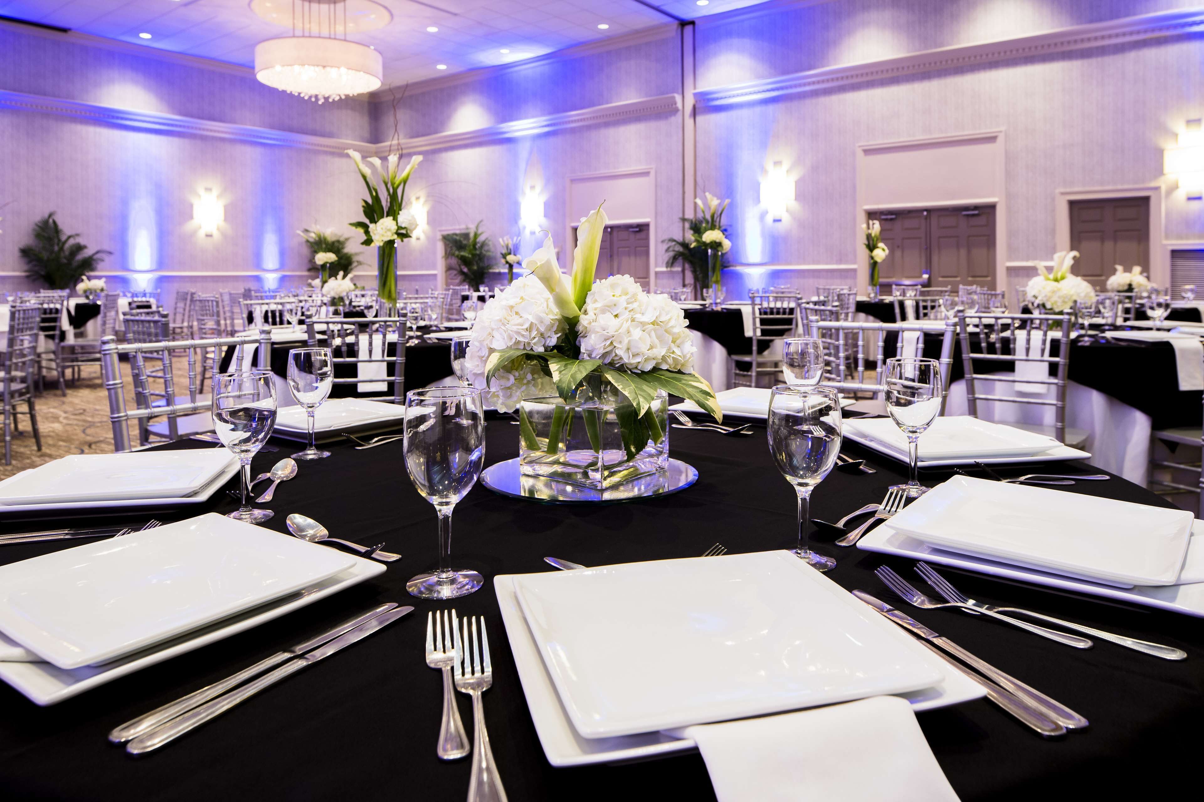 Un salón de banquetes con mesas redondas dispuestas para cenar, con manteles blancos, cubiertos y centros de mesa florales.