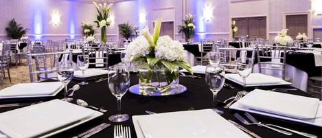 Un salón de banquetes con mesas redondas dispuestas para cenar, con manteles blancos, cubiertos y centros de mesa florales.