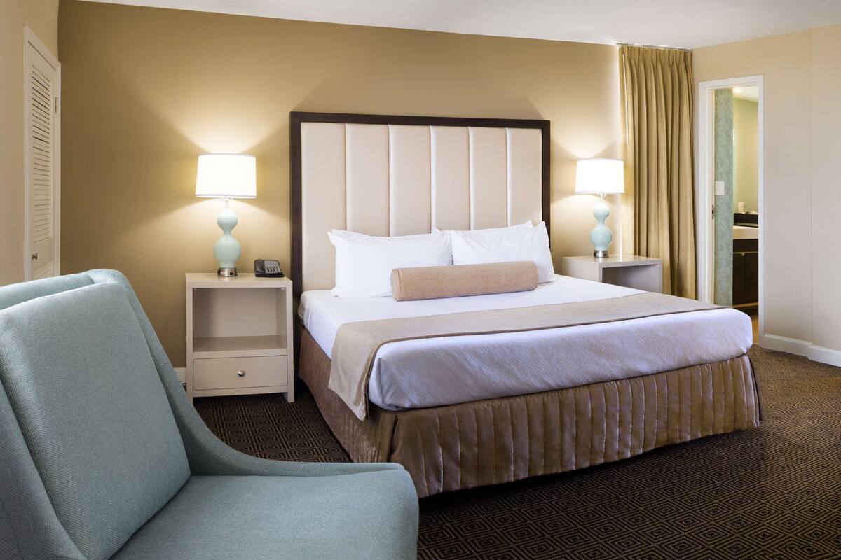 Une chambre d’hôtel avec un grand lit, deux tables de chevet avec des lampes, une chaise et une moquette à motifs.