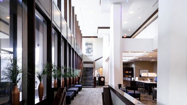 Un moderno vestíbulo de hotel con una escalera central, zonas de estar y un mostrador de recepción.