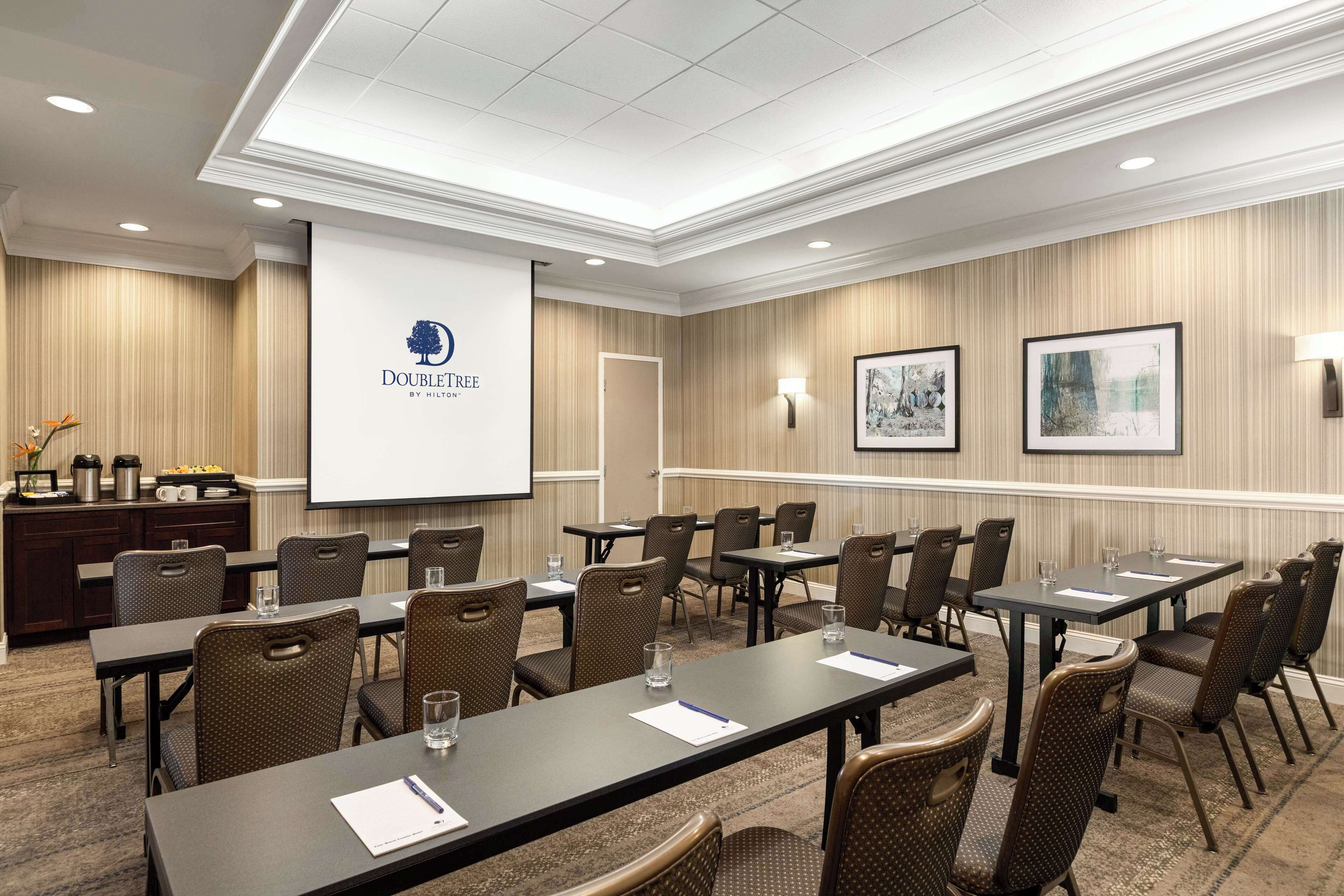 Une salle de conférence dotée d’un grand écran affichant le logo « DOUBLE TREE BY HILTON », de plusieurs tables avec des chaises et d’œuvres d’art encadrées accrochées aux murs.