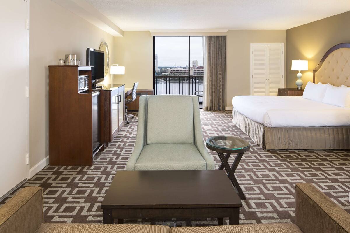 Une chambre d’hôtel avec un lit, un bureau avec une télévision, une chaise, une petite table et une vue sur la ville par la fenêtre.