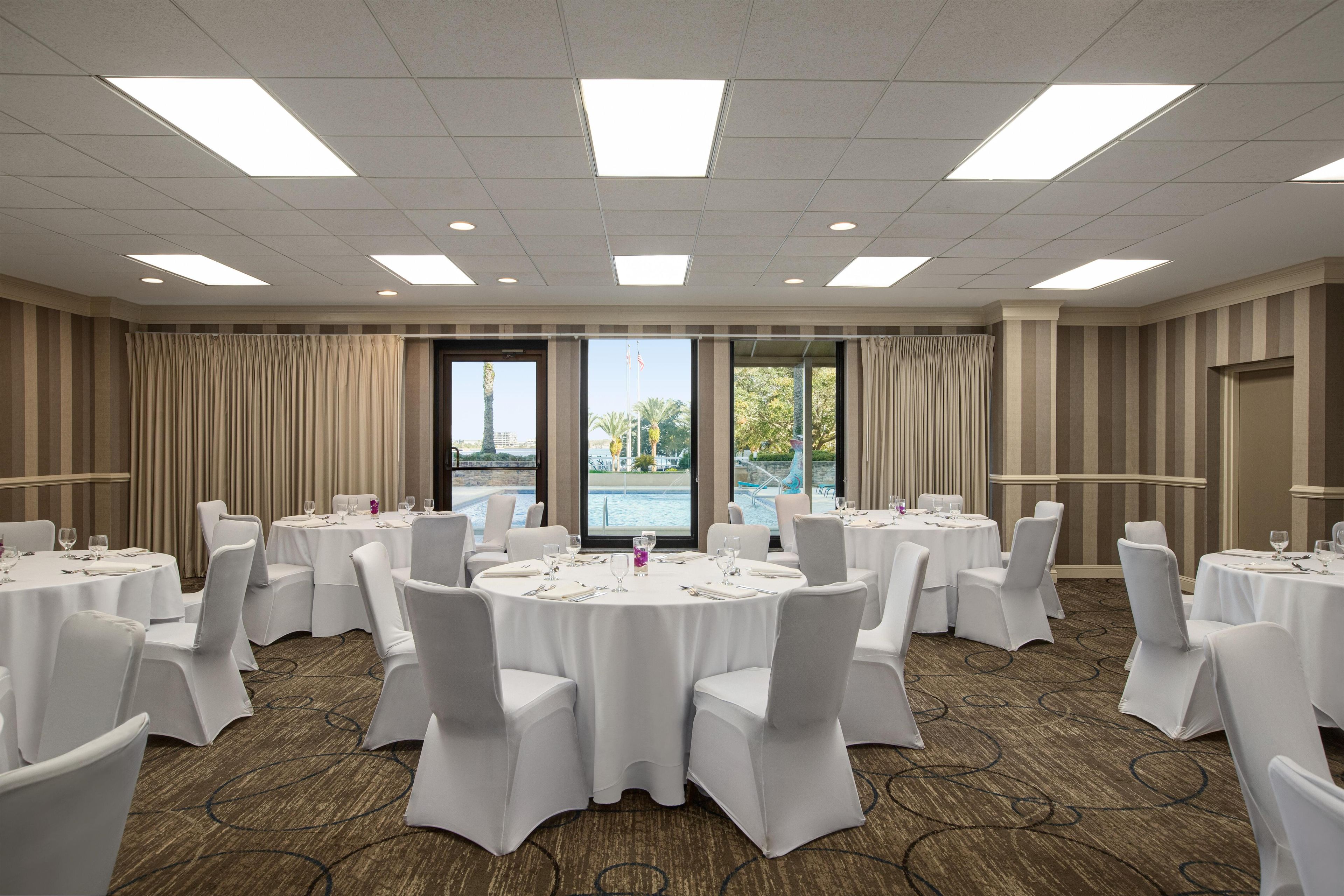 A conference room with multiple tables, chairs, and a large window overlooking a pool.
