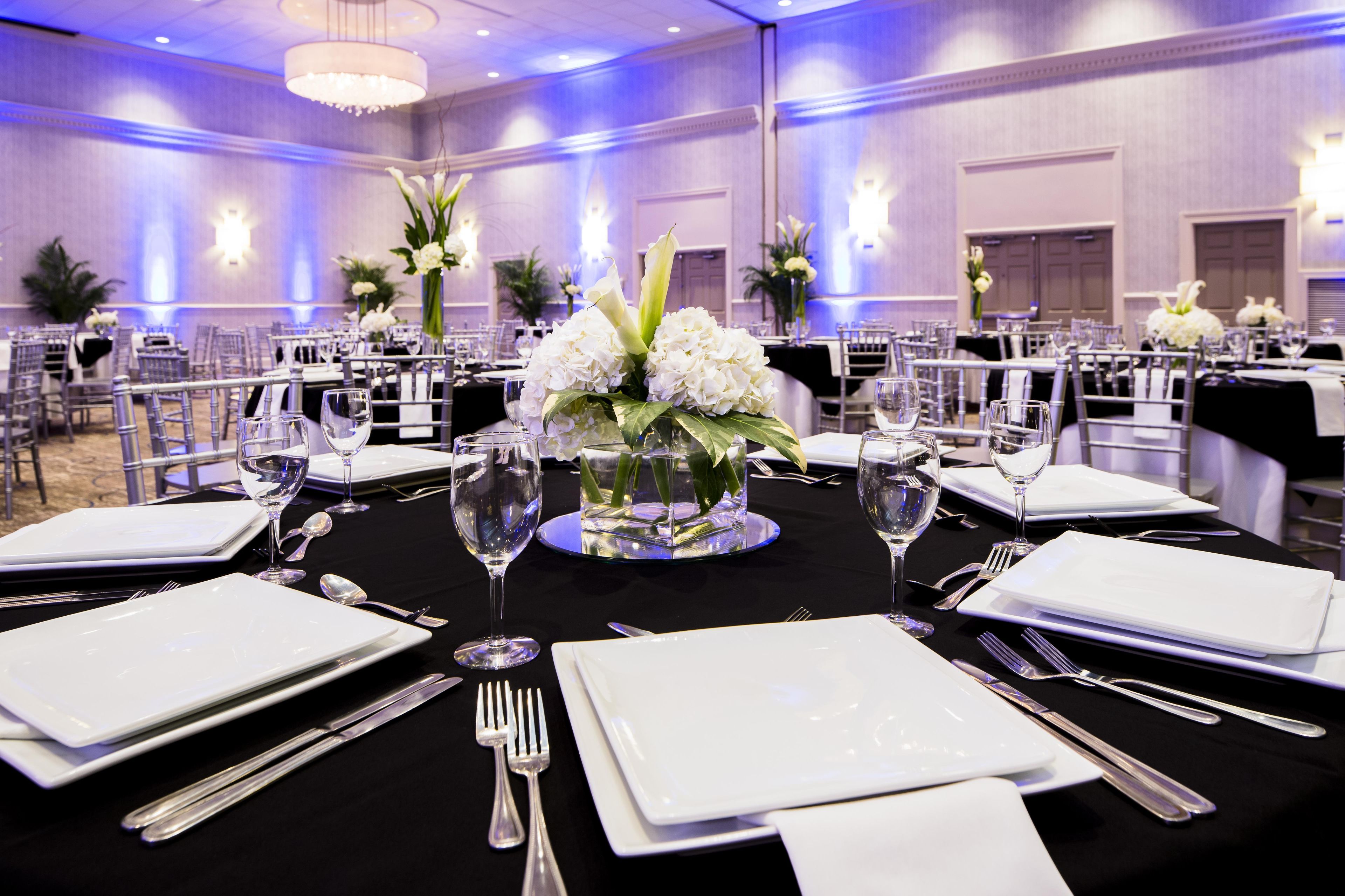 A banquet hall with round tables set for a formal event, complete with white tablecloths, silverware, and glassware.