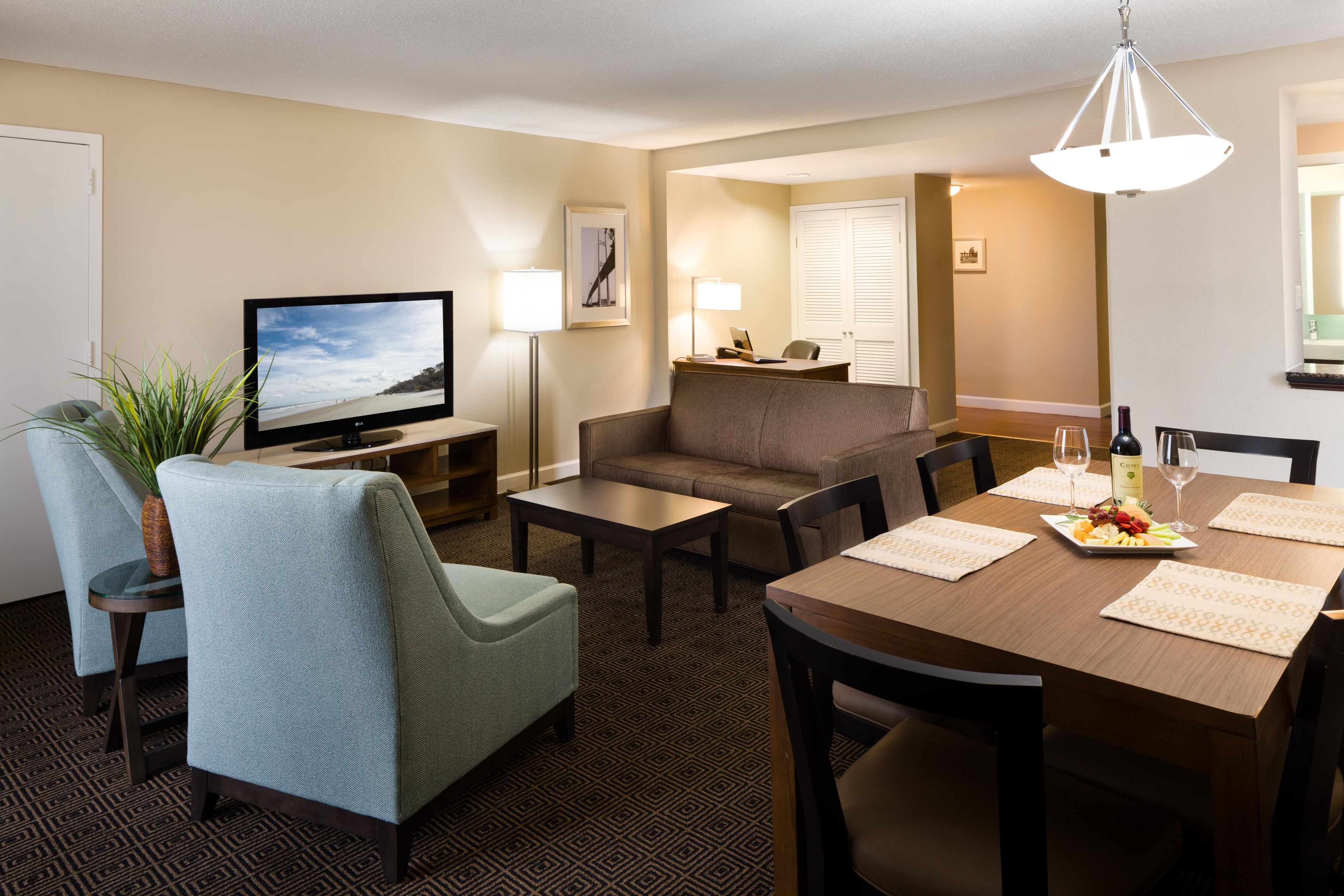 Habitación de hotel con televisor, zona de estar, mesa de comedor y una lámpara.